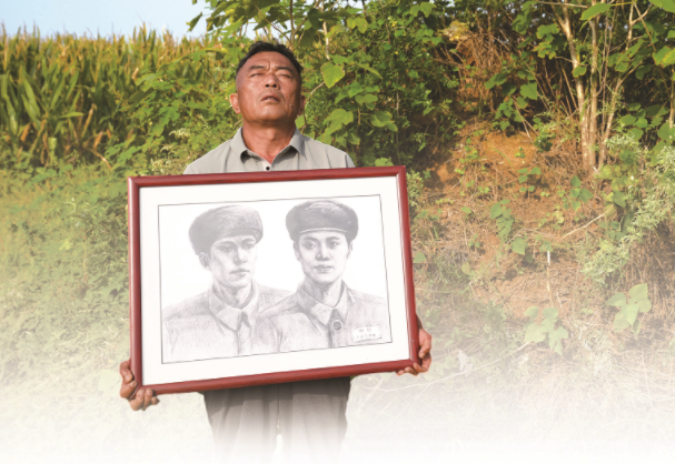 陳為村抱著烈士陳淑彬兄弟倆的畫像，在太爺爺太奶奶墳前百感交集。